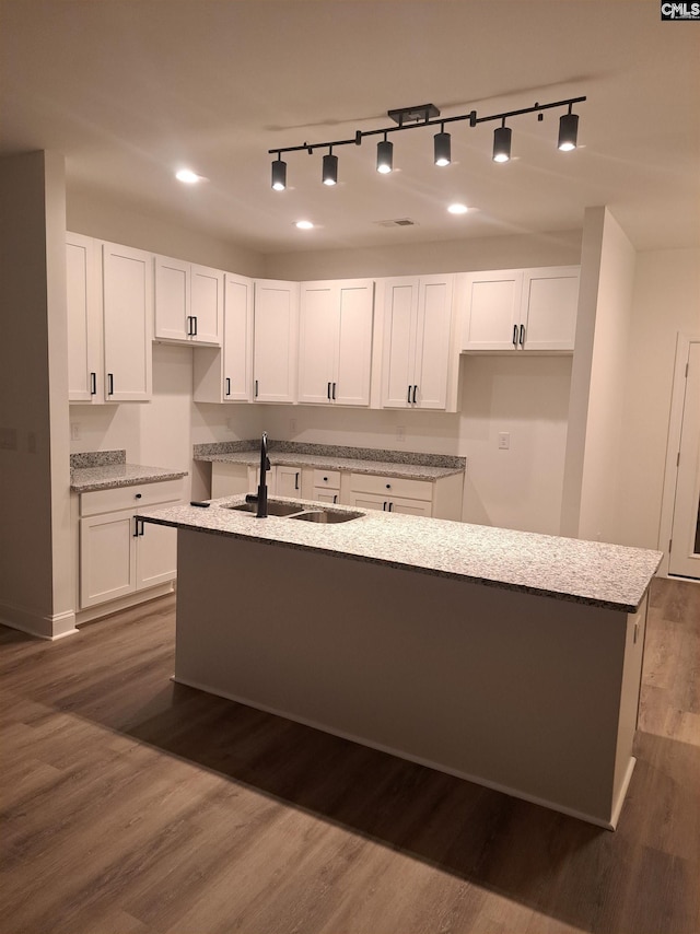 kitchen featuring white cabinetry, an island with sink, sink, dark hardwood / wood-style flooring, and light stone countertops