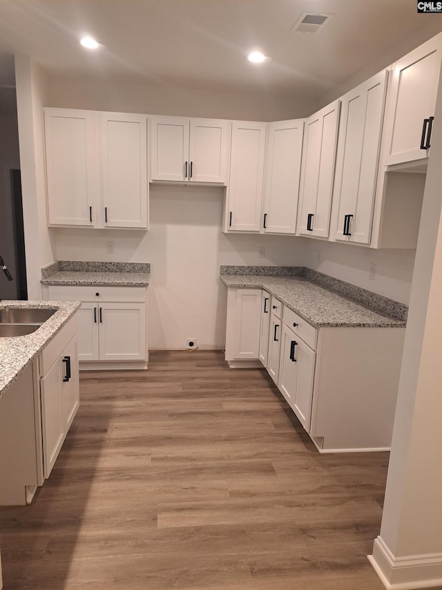 kitchen with light stone countertops, sink, light hardwood / wood-style flooring, and white cabinets