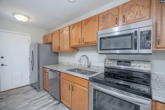 kitchen with appliances with stainless steel finishes, light hardwood / wood-style floors, light stone counters, and sink