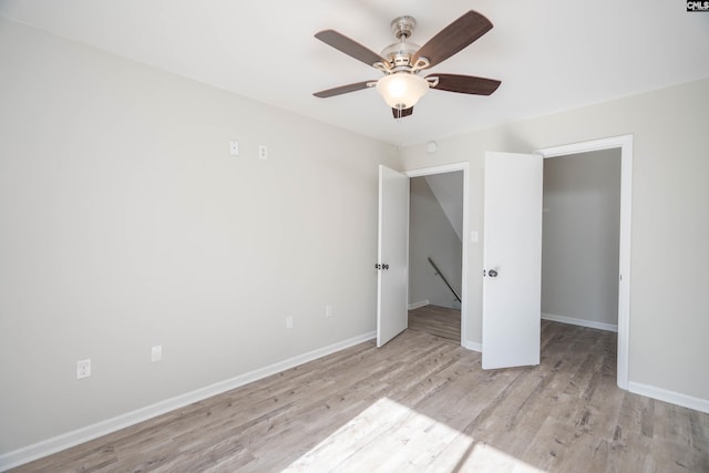 unfurnished bedroom with a spacious closet, a closet, ceiling fan, and light wood-type flooring