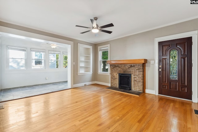 unfurnished living room with a brick fireplace, ornamental molding, light hardwood / wood-style flooring, and built in shelves