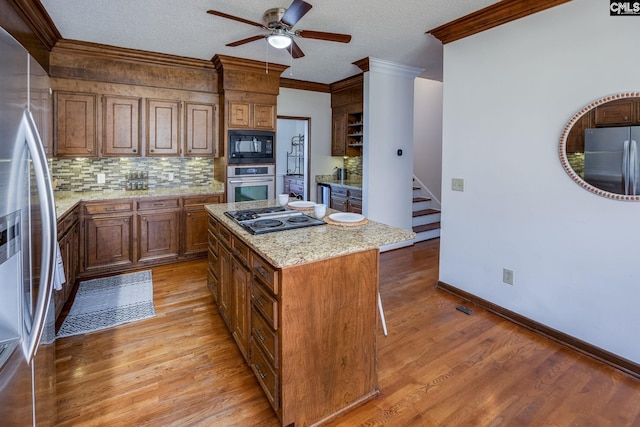 kitchen with black appliances, a kitchen island, light wood-type flooring, light stone counters, and crown molding