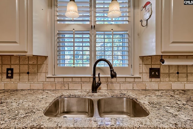 interior details with tasteful backsplash, sink, light stone countertops, and white cabinets