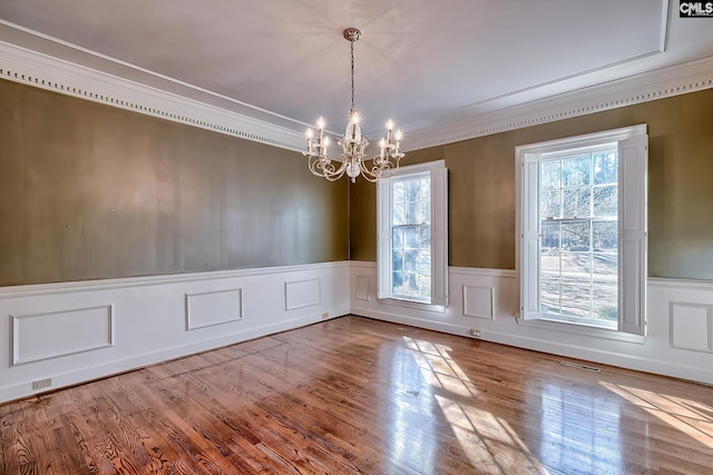 unfurnished dining area with hardwood / wood-style flooring, ornamental molding, and a chandelier