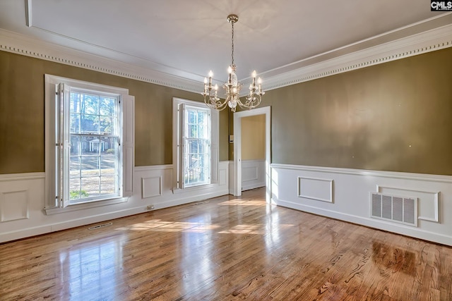 unfurnished dining area featuring an inviting chandelier, crown molding, and wood-type flooring