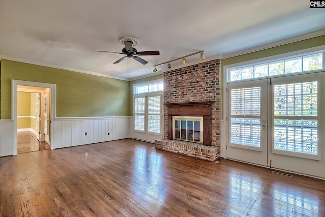 unfurnished living room with a fireplace, hardwood / wood-style flooring, ceiling fan, crown molding, and track lighting