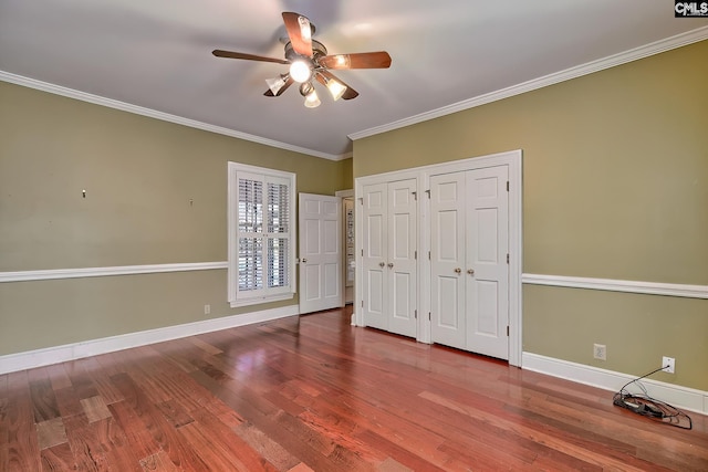 unfurnished bedroom featuring hardwood / wood-style floors, ornamental molding, multiple closets, and ceiling fan