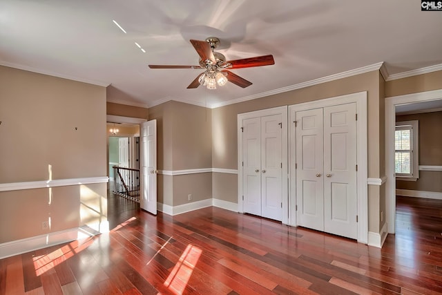 unfurnished bedroom featuring ceiling fan, crown molding, dark hardwood / wood-style floors, and multiple closets