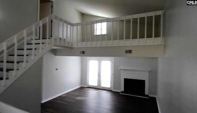 unfurnished living room with dark wood-type flooring, a towering ceiling, and french doors