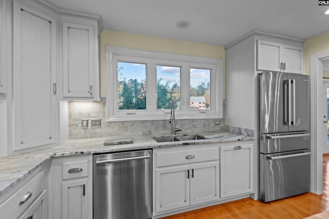 kitchen with light stone countertops, stainless steel appliances, light hardwood / wood-style floors, sink, and backsplash