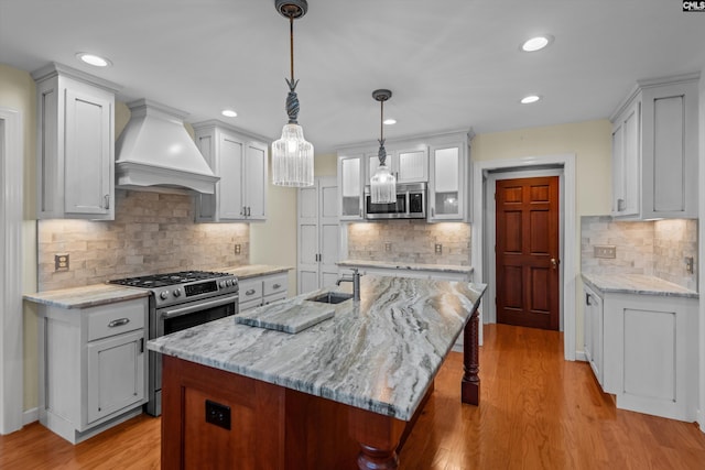 kitchen featuring an island with sink, hanging light fixtures, stainless steel appliances, and custom exhaust hood