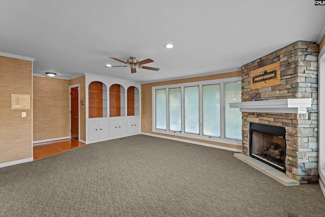 unfurnished living room with ceiling fan, ornamental molding, carpet flooring, and a stone fireplace