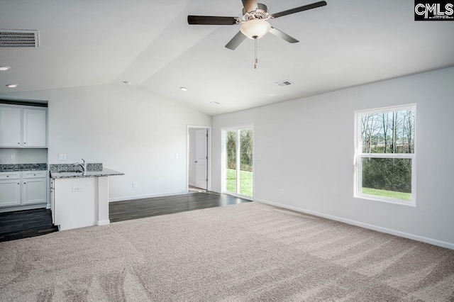 unfurnished living room with vaulted ceiling, ceiling fan, a healthy amount of sunlight, and dark carpet