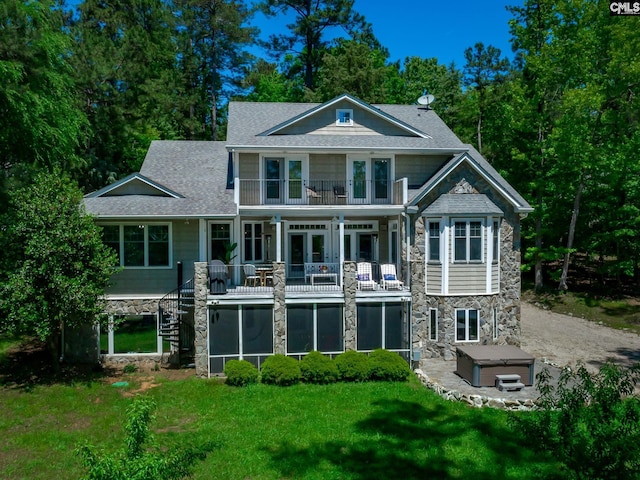 rear view of property featuring a lawn, french doors, a hot tub, and a balcony