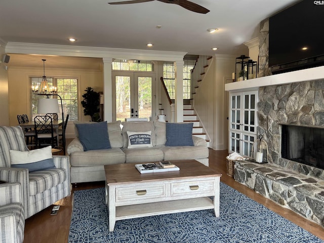 living room featuring ceiling fan with notable chandelier, dark hardwood / wood-style flooring, a stone fireplace, french doors, and ornamental molding