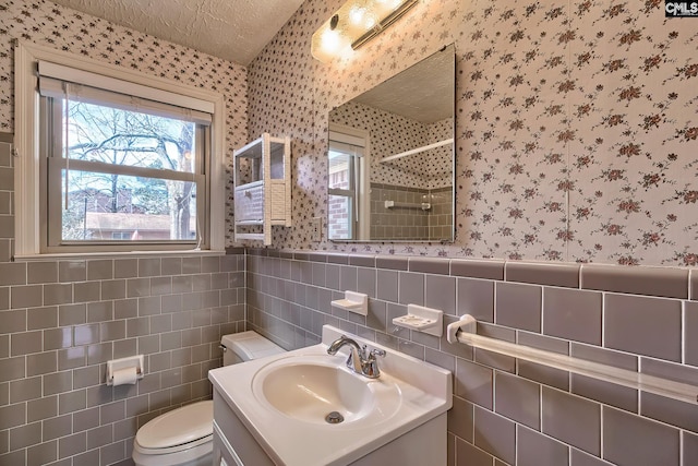 bathroom featuring walk in shower, vanity, tile walls, toilet, and a textured ceiling