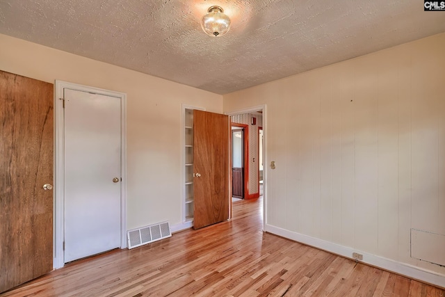 unfurnished bedroom with light wood-type flooring, a textured ceiling, and wooden walls