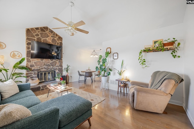 living room with vaulted ceiling, light wood-type flooring, ceiling fan with notable chandelier, and a stone fireplace