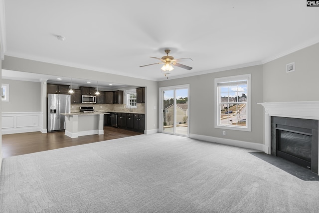 unfurnished living room featuring ceiling fan, ornamental molding, and dark colored carpet