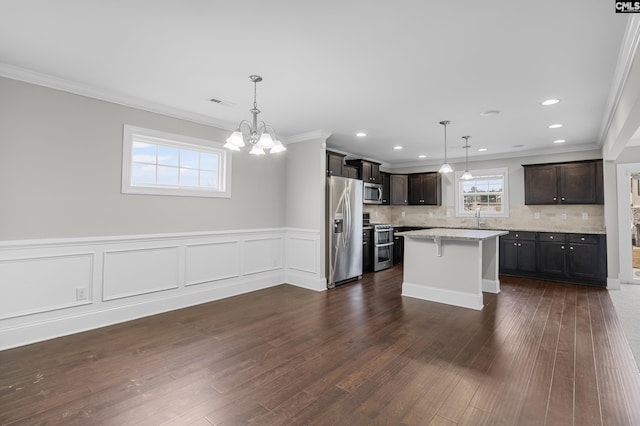 kitchen with tasteful backsplash, a notable chandelier, a kitchen island, hanging light fixtures, and appliances with stainless steel finishes