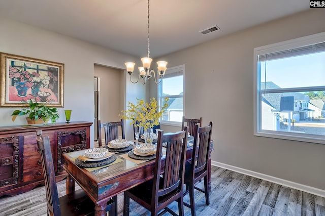 dining area with wood-type flooring, a notable chandelier, and a healthy amount of sunlight