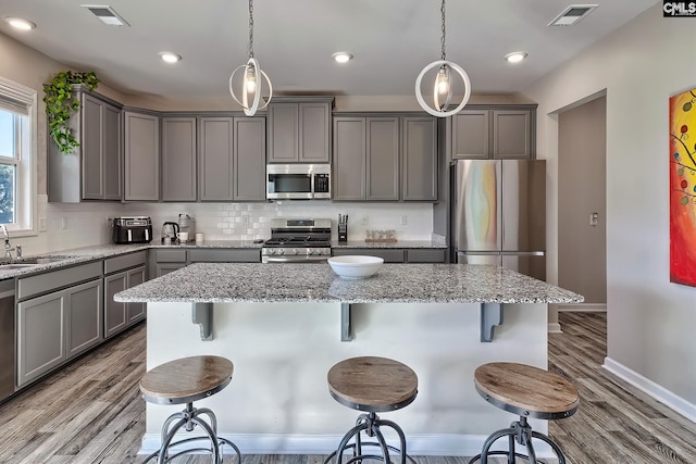 kitchen featuring a breakfast bar, gray cabinetry, stainless steel appliances, and pendant lighting