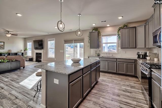 kitchen featuring appliances with stainless steel finishes, a center island, decorative light fixtures, sink, and light stone counters