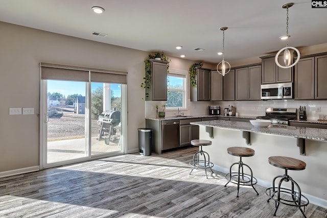 kitchen featuring decorative light fixtures, sink, light hardwood / wood-style flooring, stainless steel appliances, and light stone counters