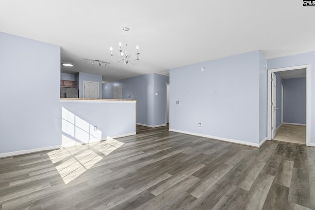 unfurnished living room with dark hardwood / wood-style floors, track lighting, and a notable chandelier