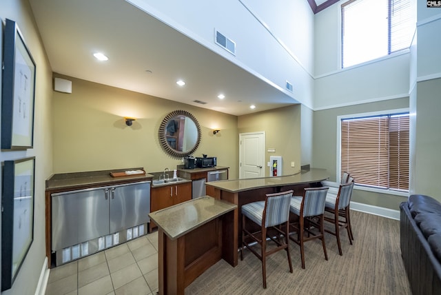 kitchen featuring dishwasher, sink, a high ceiling, a kitchen breakfast bar, and light tile patterned floors