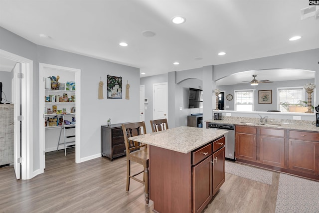 kitchen with a kitchen bar, ceiling fan, a center island, stainless steel dishwasher, and sink