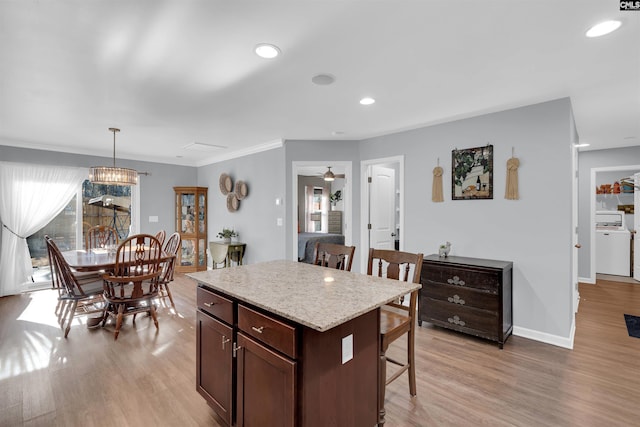 kitchen featuring ceiling fan with notable chandelier, dark brown cabinetry, a kitchen island, hanging light fixtures, and a breakfast bar area