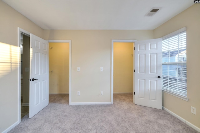 unfurnished bedroom with a spacious closet, a closet, and light colored carpet