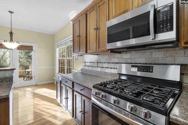 kitchen with decorative light fixtures, backsplash, light hardwood / wood-style floors, crown molding, and appliances with stainless steel finishes