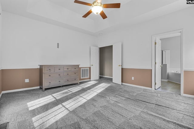 unfurnished bedroom featuring ceiling fan, ensuite bathroom, light colored carpet, and a tray ceiling