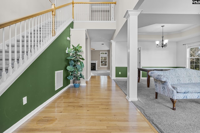 foyer entrance featuring hardwood / wood-style flooring, ornate columns, ornamental molding, and a chandelier