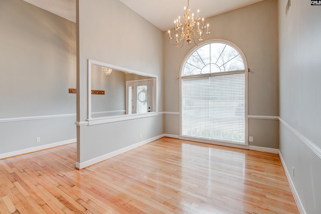 spare room with a high ceiling, baseboards, an inviting chandelier, and wood finished floors