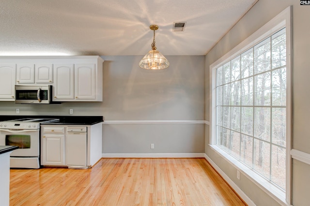 kitchen with white range with electric stovetop, dark countertops, stainless steel microwave, white cabinetry, and plenty of natural light