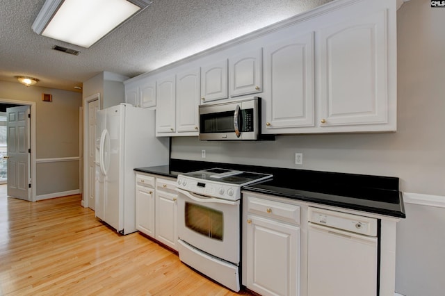 kitchen with white appliances, dark countertops, visible vents, and white cabinets