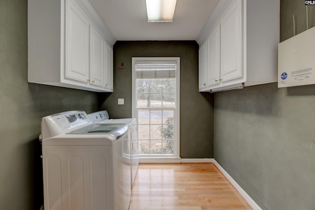 laundry room with baseboards, washing machine and clothes dryer, cabinet space, and light wood-style floors