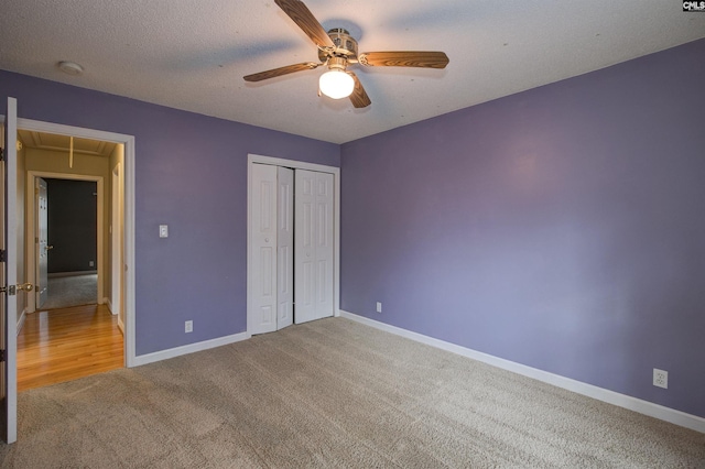 unfurnished bedroom with a textured ceiling, carpet, attic access, and baseboards