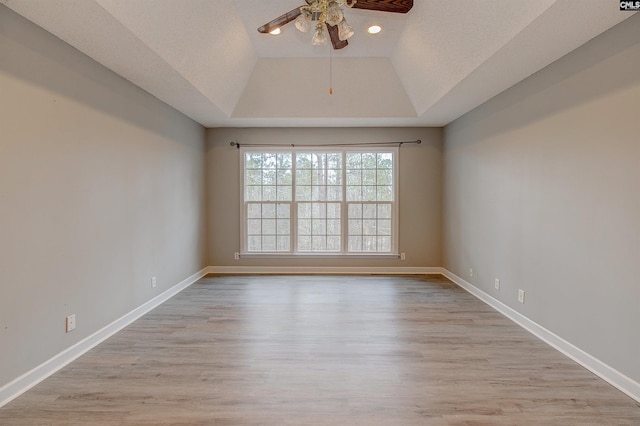 empty room with baseboards, a ceiling fan, lofted ceiling, a tray ceiling, and light wood-type flooring