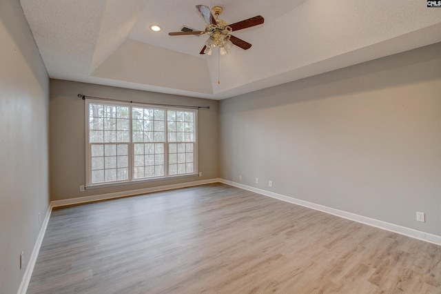 spare room with ceiling fan, a textured ceiling, a raised ceiling, and light wood-type flooring