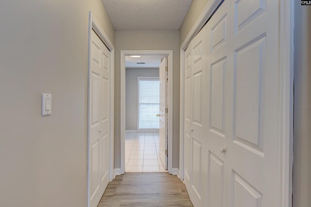 hall with light wood-style flooring, baseboards, and a textured ceiling