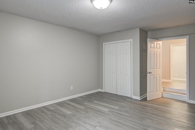 unfurnished bedroom with a closet, a textured ceiling, baseboards, and wood finished floors