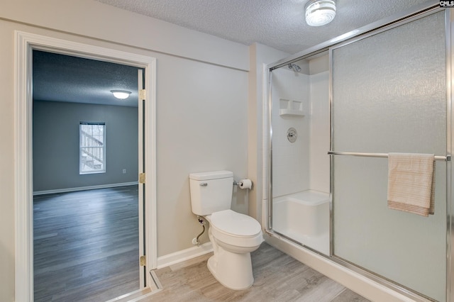 bathroom with toilet, a stall shower, a textured ceiling, wood finished floors, and baseboards