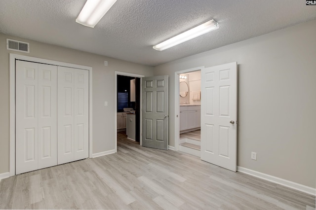 unfurnished bedroom featuring light wood-style floors, a textured ceiling, visible vents, and a closet