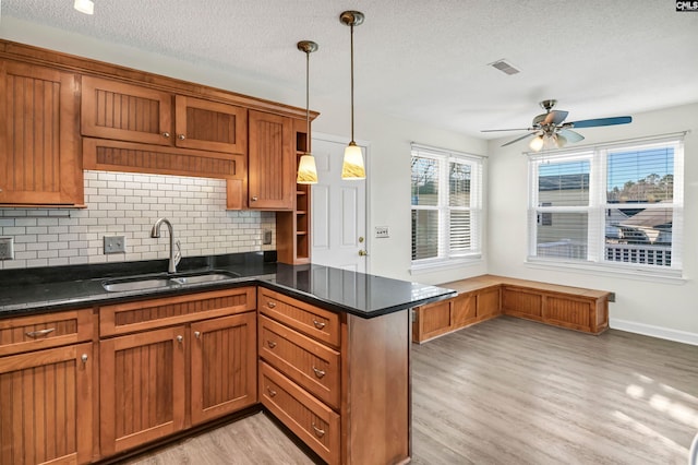 kitchen with ceiling fan, backsplash, kitchen peninsula, sink, and hanging light fixtures