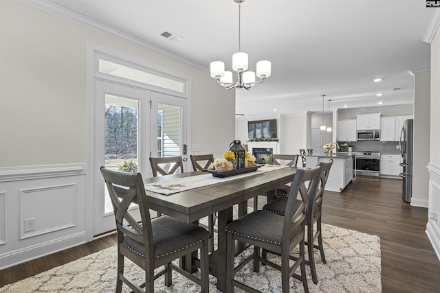 dining area with dark wood-style flooring, a glass covered fireplace, visible vents, and crown molding