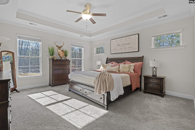 carpeted bedroom with ornamental molding, a tray ceiling, visible vents, and baseboards